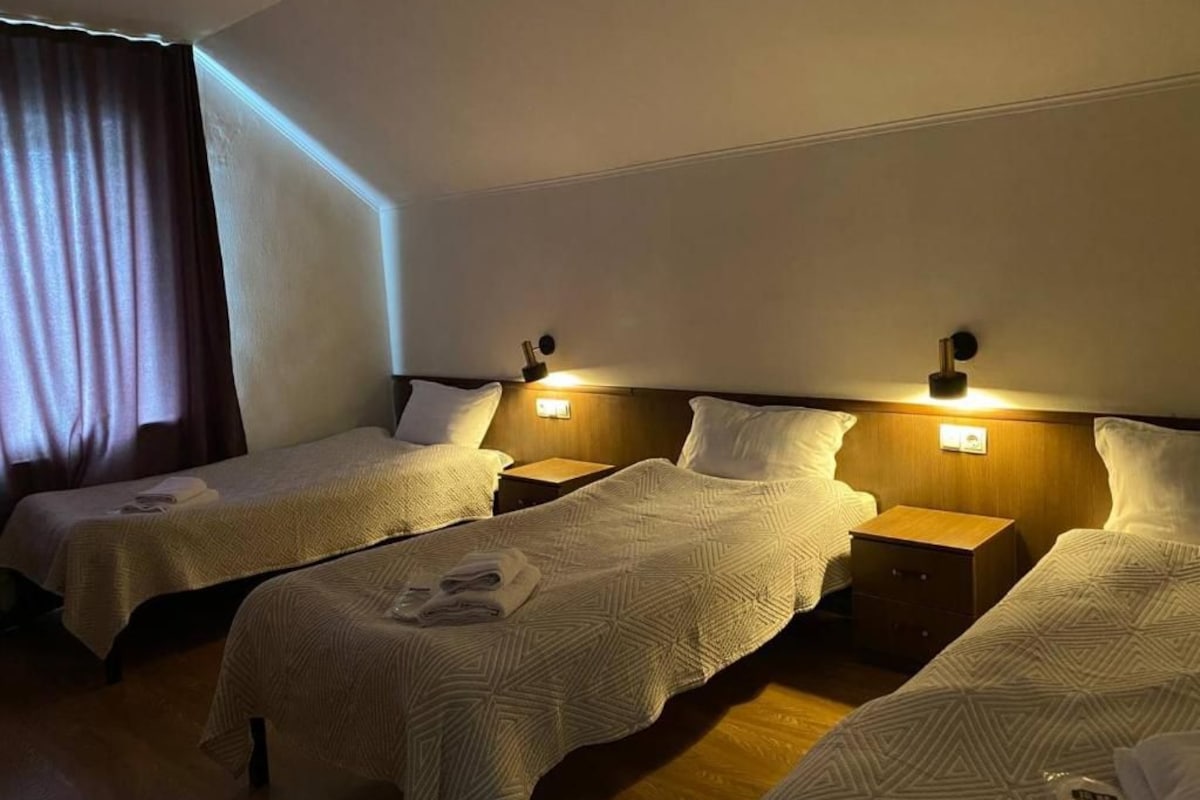 Ein Hotelzimmer mit drei Einzelbetten, jeweils mit einem hölzernen Kopfteil und Nachttischen.