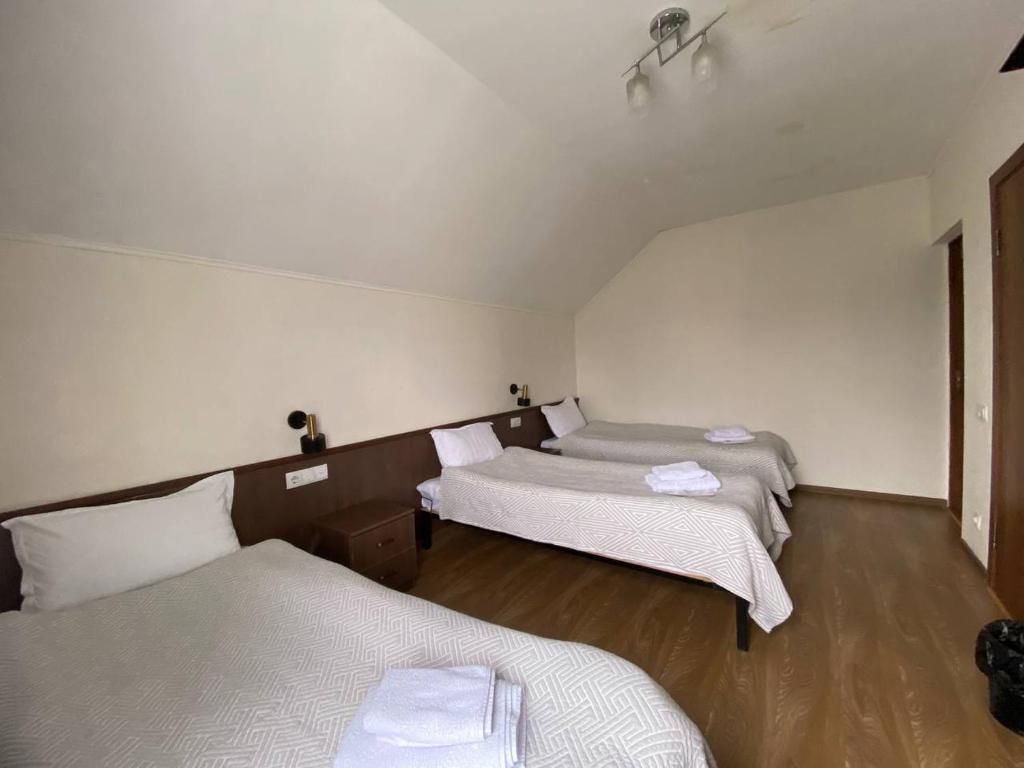 A hotel room with three beds, wooden flooring, and a simple, clean design.