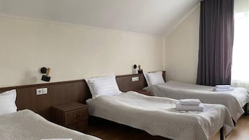 Habitación de hotel con dos camas individuales, una mesita de noche, una lámpara y un ventanal con cortinas.