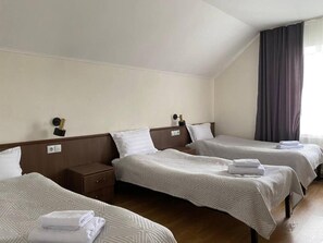 Ein Hotelzimmer mit zwei Einzelbetten, einem Nachttisch, einer Lampe und einem Fenster mit Vorhängen.