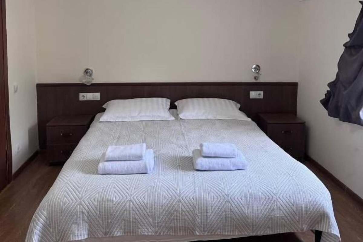 Ein Einzelbett mit einem gemusterten Bettüberwurf, zwei Nachttische und eine Deckenleuchte.