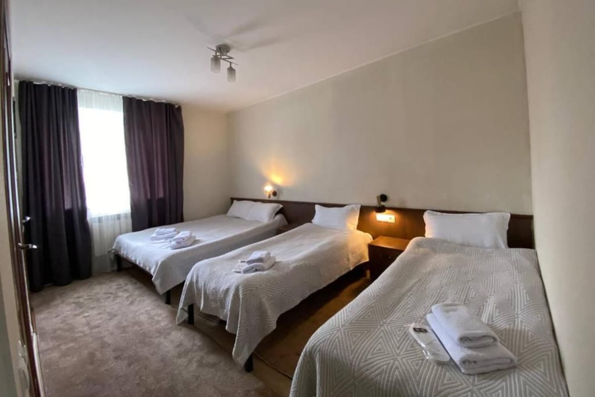 Ein Hotelzimmer mit drei Einzelbetten, einem Deckenventilator und einem fenster mit Vorhängen.