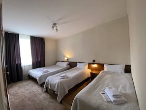 Ein Hotelzimmer mit drei Einzelbetten, einem Deckenventilator und einem fenster mit Vorhängen.