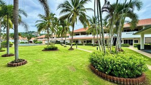 Pátio de hotel com palmeiras, piscina e edifício com telhado vermelho.