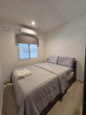 A bedroom with a bed, a window with blinds, an air conditioning unit, and a tiled floor. - 2BR Condo Near City Center (NG430) (Hua Hin)