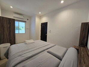 Quarto de hotel com cama, janela, aparelho de ar condicionado e porta.