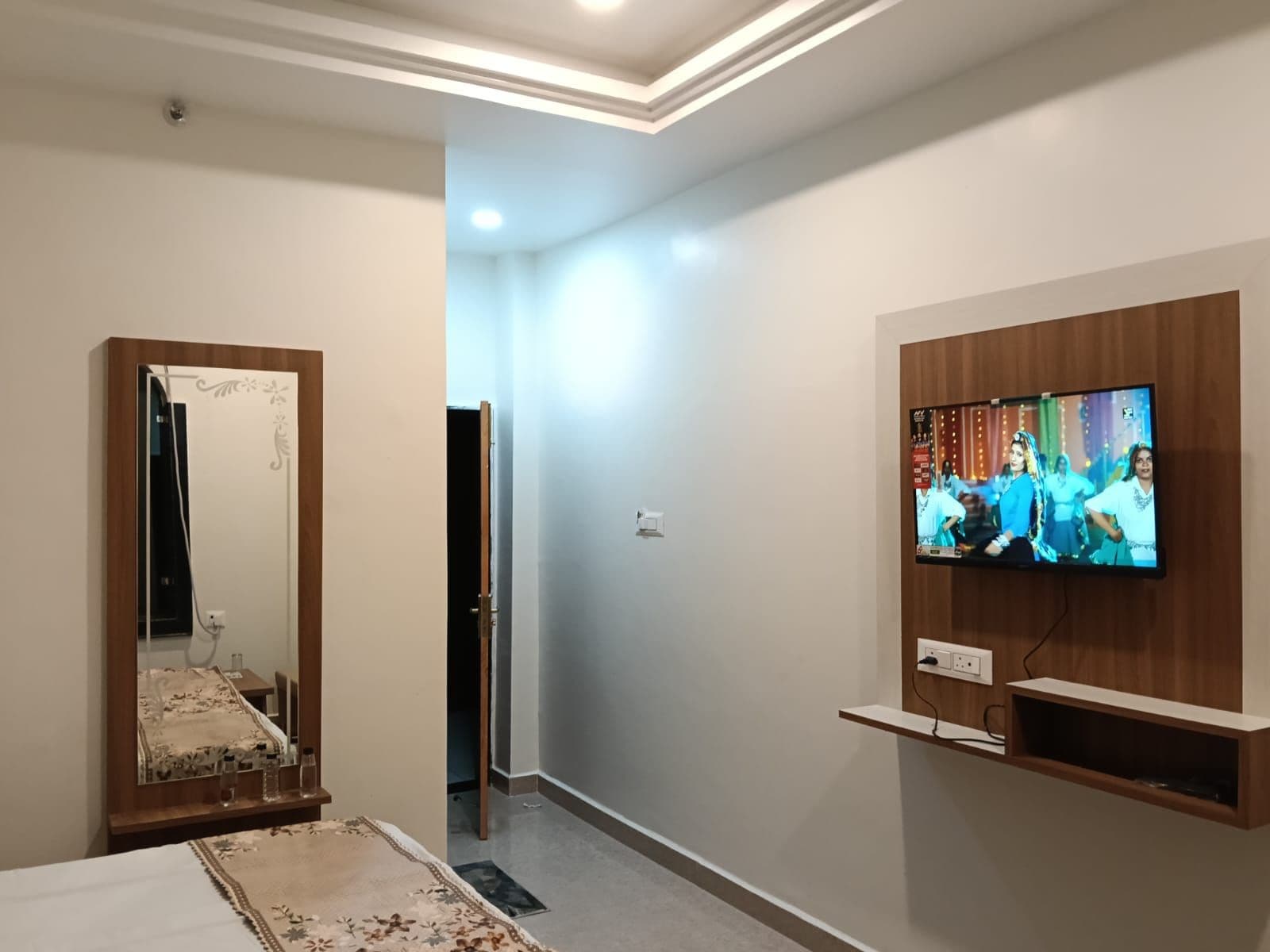 A hotel room with a television mounted on the wall, a mirror, and a bed.