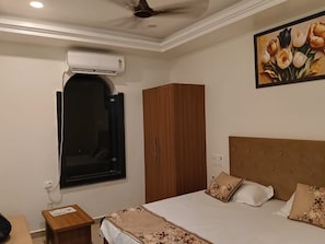 A bedroom with a bed, a wardrobe, an air conditioning unit, a window, and a painting on the wall.