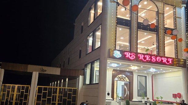 Ein mehrstöckiges Gebäude mit einem auffälligen 'RS RESORT' Schild, einem befahrtsbeschränkten Eingangsbereich und einer gepflasterten Fläche mit abgestellten Motorrädern.