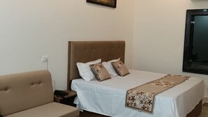 Ein Hotelzimmer mit einem Bett, einer Couch, einem kleinen Holztisch, einem Deckenventilator, einer Klimaanlage und einem an der Wand befestigten Fernseher.