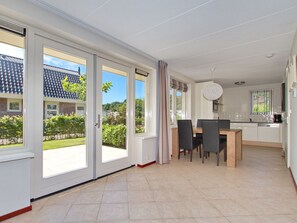 A modern kitchen with a dining area, large sliding glass doors leading to a garden, and a view of a house with a tiled roof. - Holiday Home With 1 Bedroom (Noordwijk)