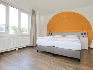 A bedroom with a bed, a nightstand, a window, and a wall with an orange arch. - Holiday Home With 1 Bedroom (Noordwijk)