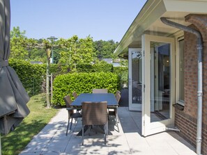 An outdoor patio with a table and chairs, a covered grill, and a glass door leading to a covered area. - Holiday Home With 1 Bedroom (Noordwijk)
