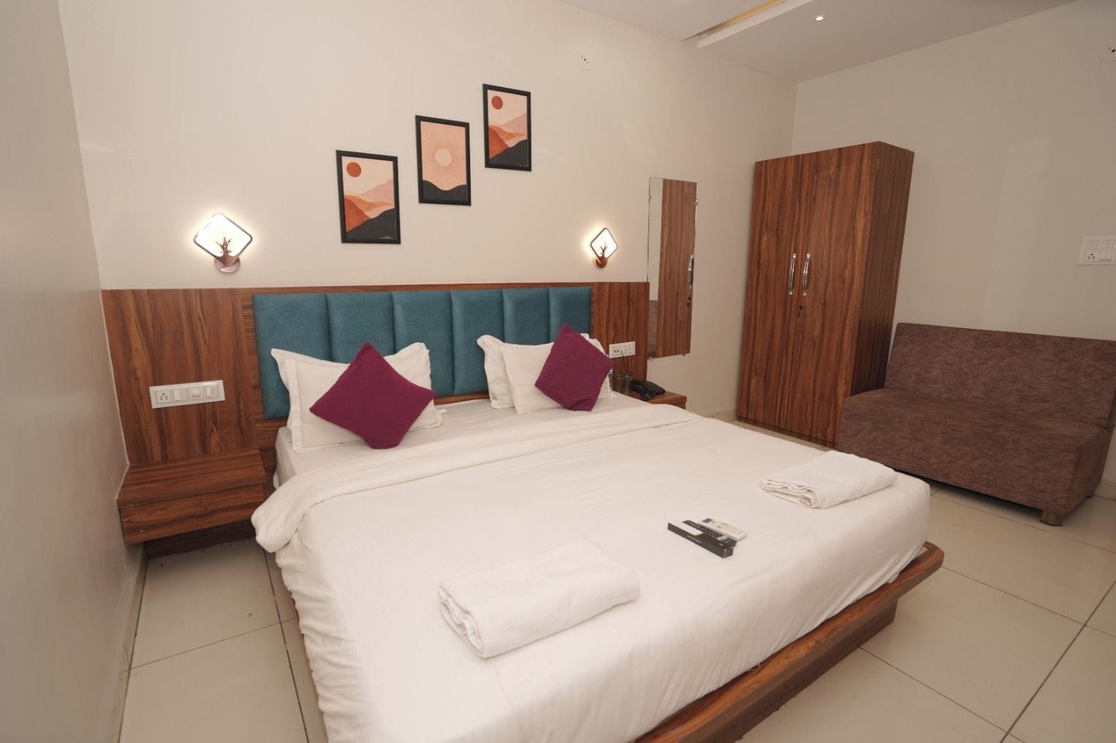 Habitación de hotel con una cama grande, cabecera de madera, dos mesitas de noche, un armario y lámparas fijadas a la pared.