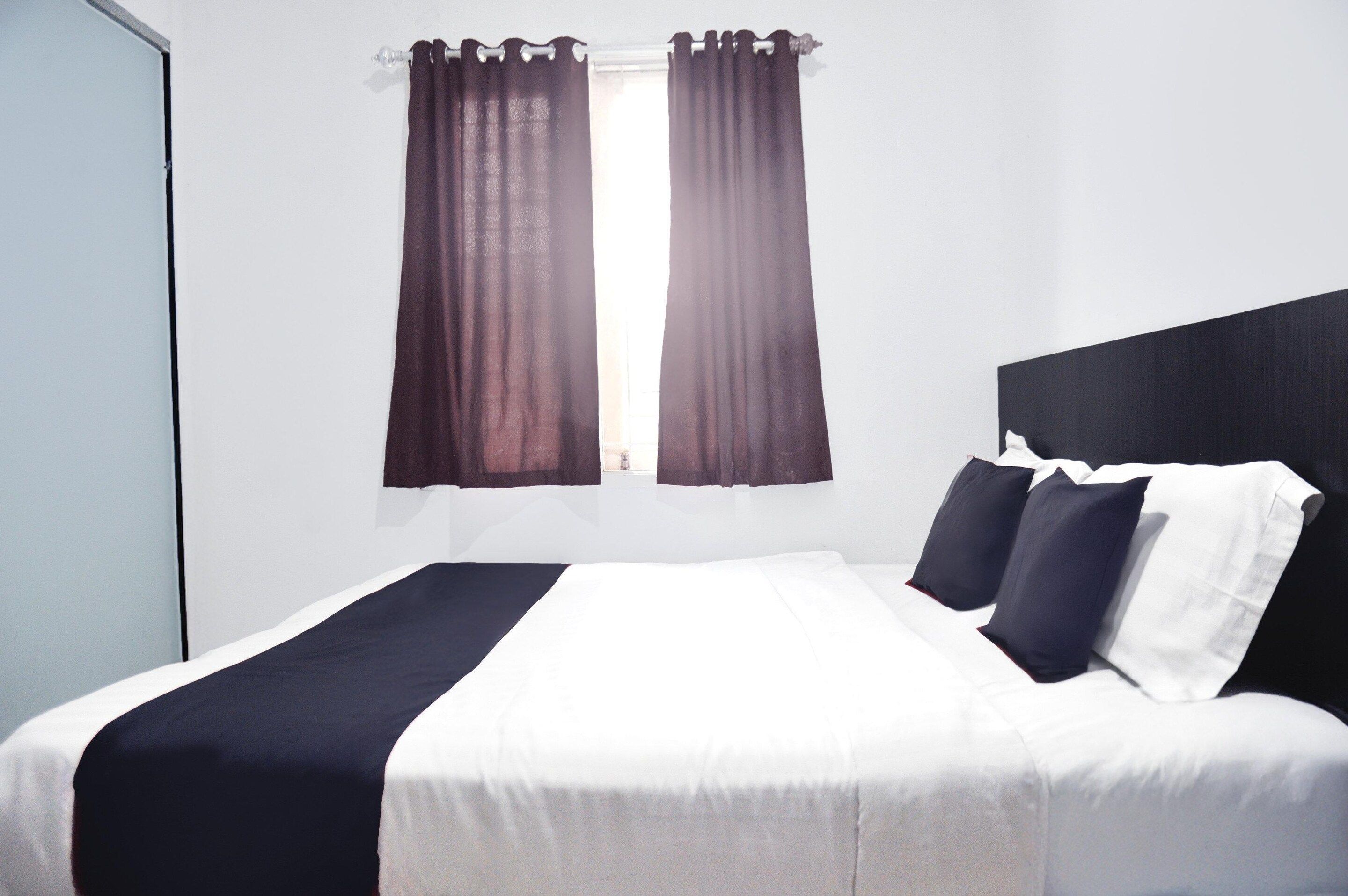 A standard hotel room with a bed, curtains, and a window.