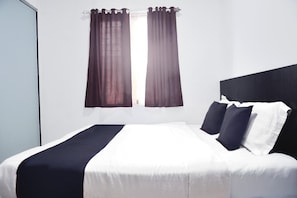 Une chambre d’hôtel standard, avec un lit, des rideaux et une fenêtre.
