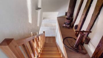 Una escalera de madera con barandilla que lleva a un rellano con pared blanca y un barril de madera.