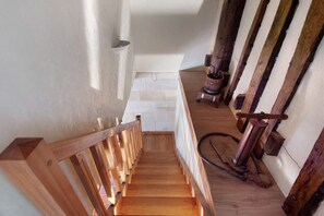 Un escalier en bois, doté d’une rampe, mène à un palier avec un mur blanc et un tonneau en bois.