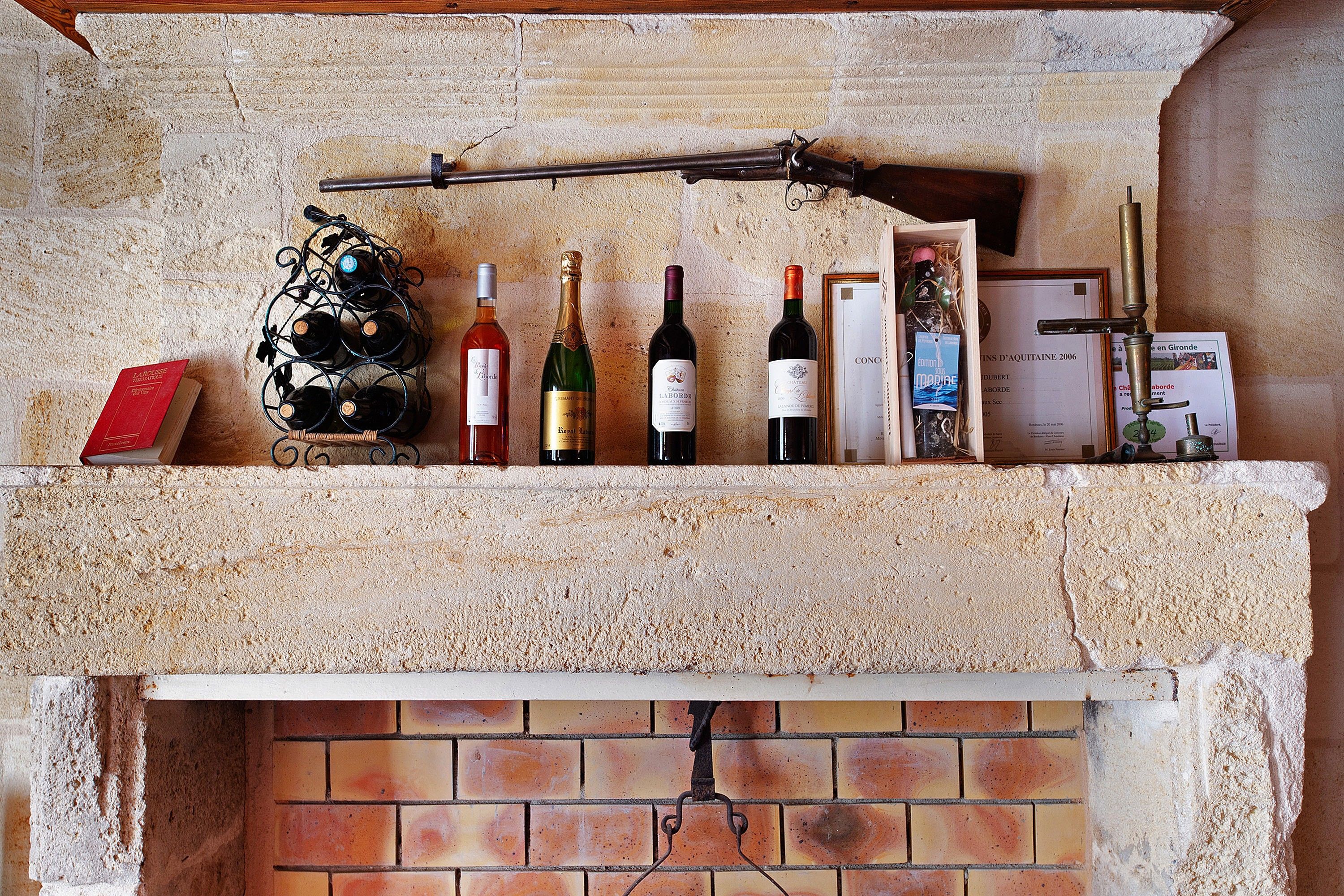A wine rack with bottles and a book on a stone fireplace mantel.