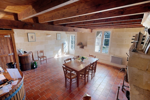 A rustic dining area with a wooden table and chairs, a brick floor, and a stone wall.