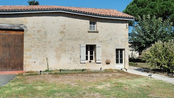 Un edificio de piedra de dos pisos con techo de tejas, una puerta de madera y contraventanas en las ventanas.