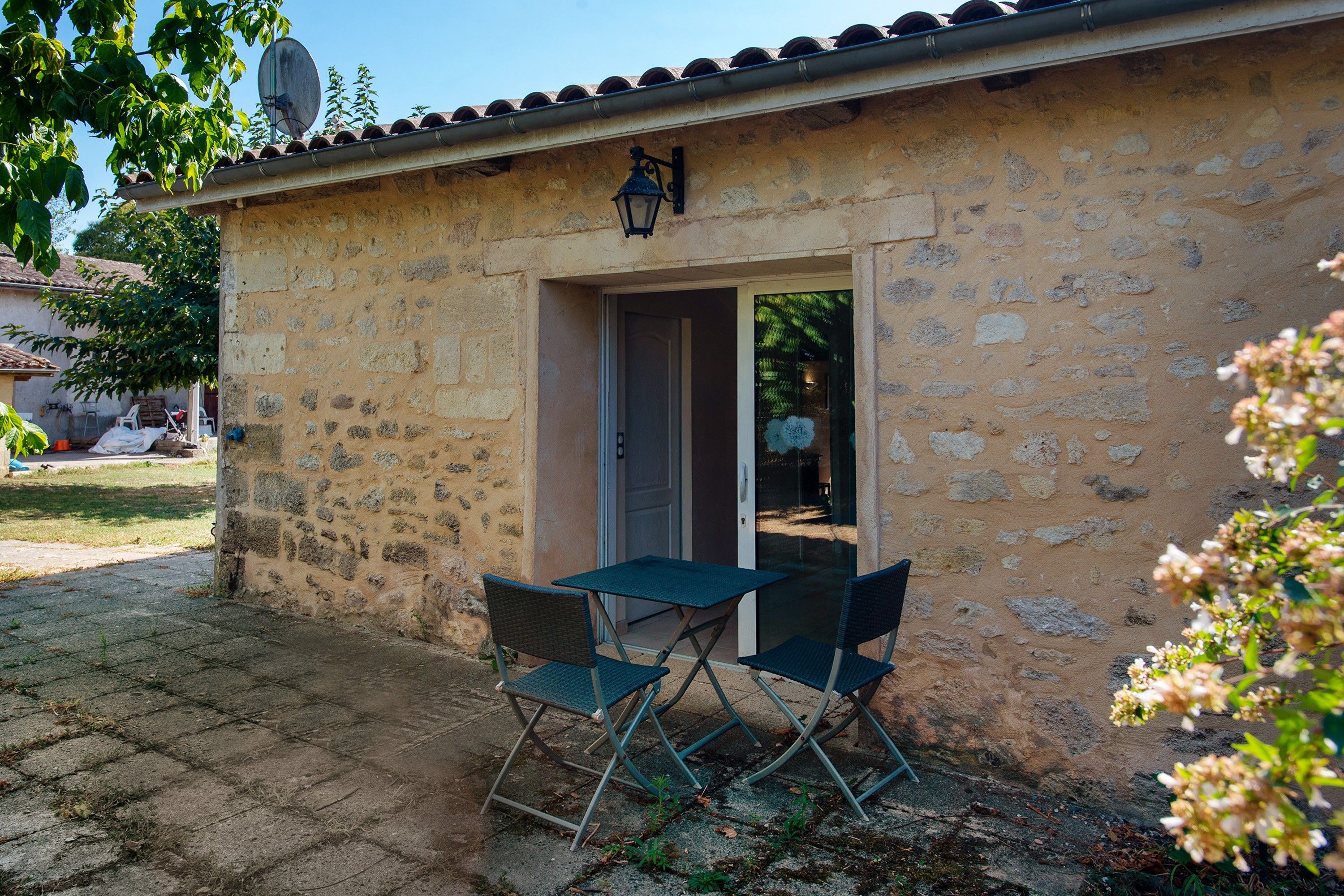 A stone building with a door and a window, a satellite dish, and a table with chairs outside.