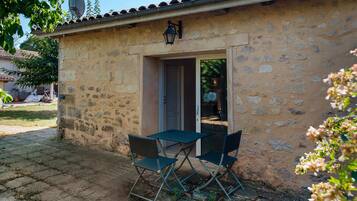 Un bâtiment en pierre avec une porte et une fenêtre, une antenne parabolique et une table avec des chaises à l’extérieur.