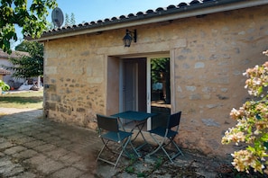 A stone building with a door and a window, a satellite dish, and a table with chairs outside.