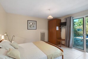 Une chambre à coucher comprenant un lit, une lampe de chevet, une armoire, un téléviseur et une porte-fenêtre coulissante donnant sur un espace extérieur.