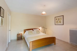 A bedroom with a wooden bed, bedside tables, a hanging lamp, a radiator, and framed artwork on the wall.