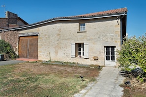 Un bâtiment rustique en pierre, avec un toit en tuiles, une porte en bois et une petite fenêtre avec des volets.