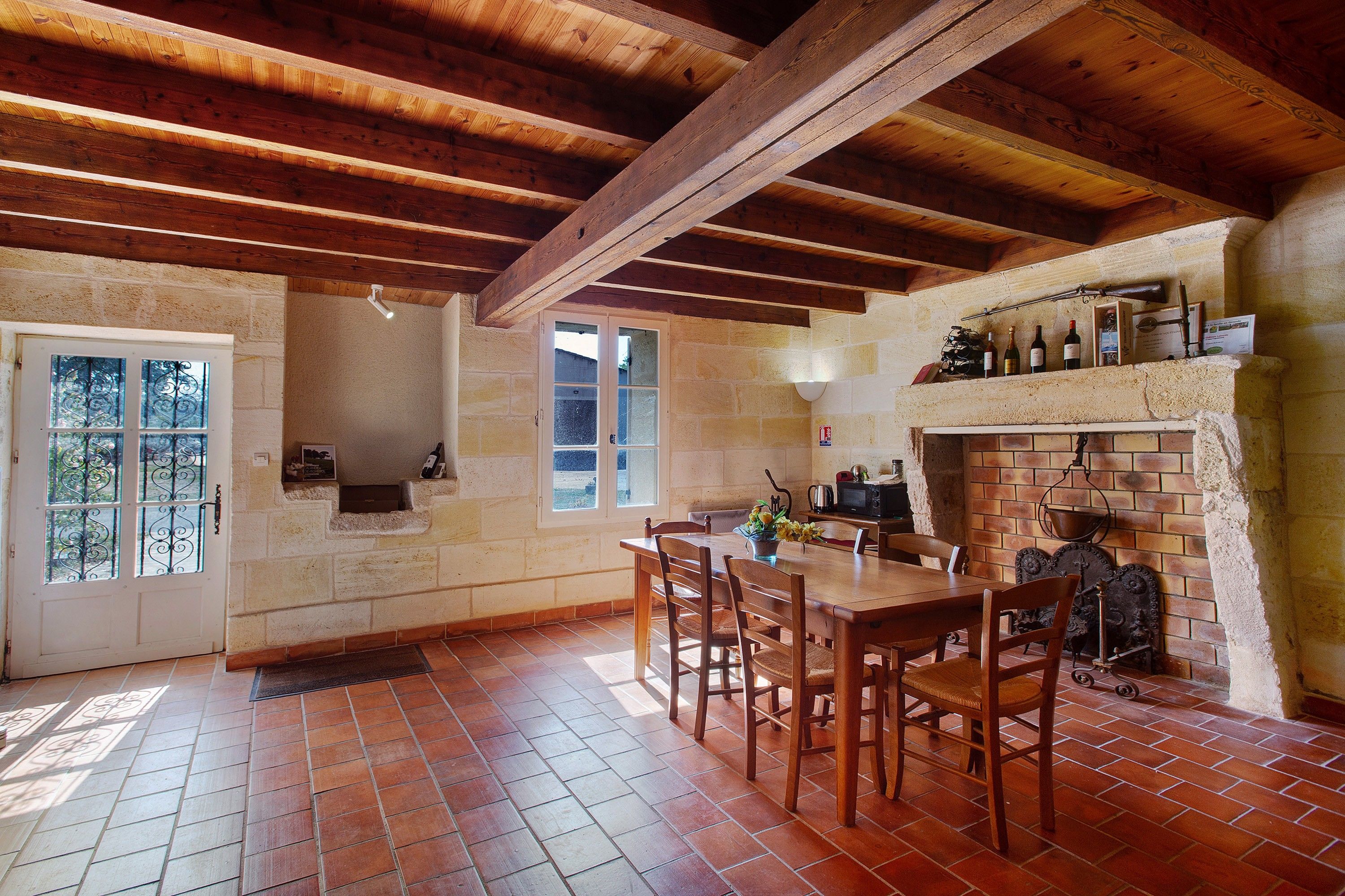 Une cuisine rustique avec une cheminée en briques, des poutres en bois et un coin repas comprenant une table et des chaises.