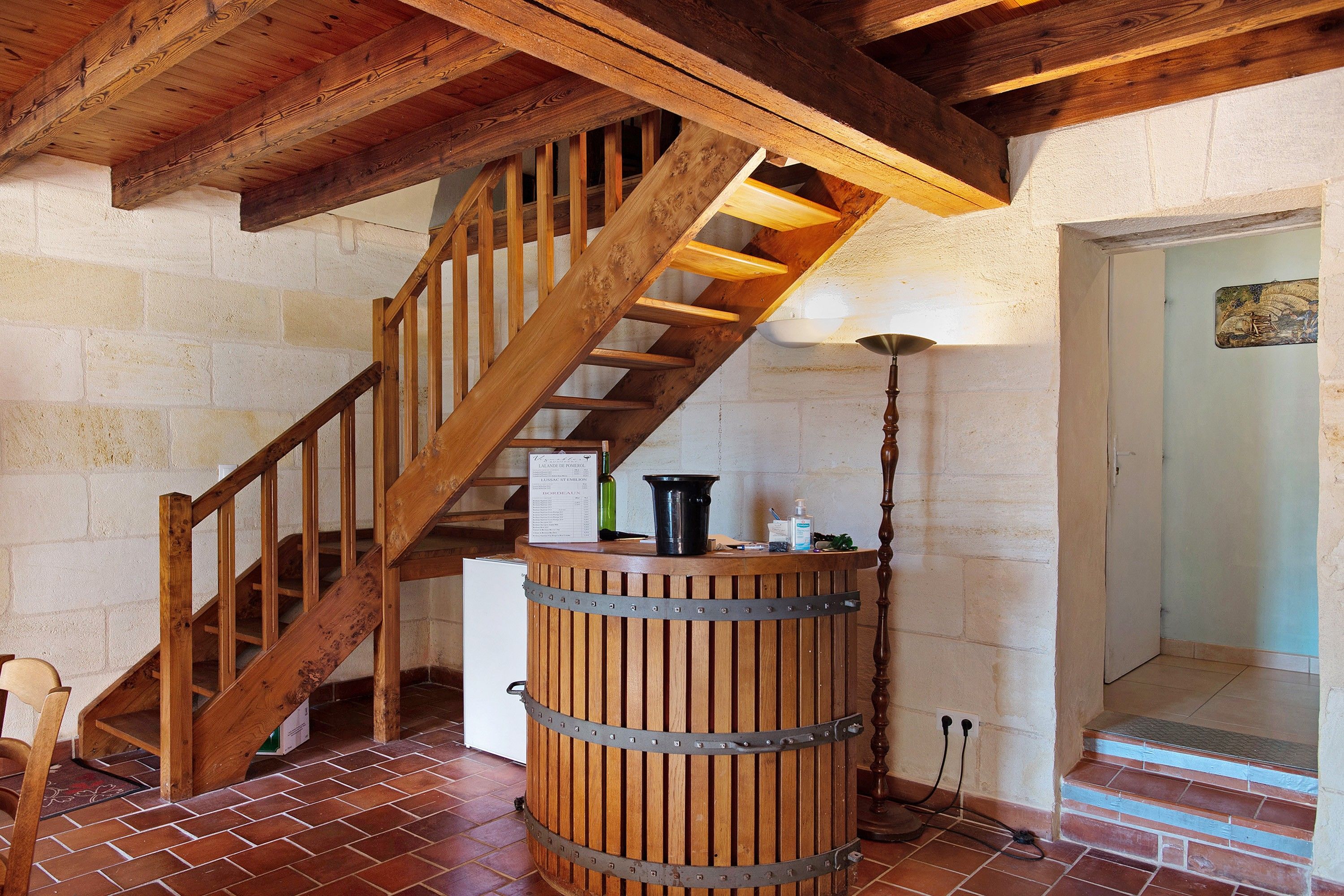 A wooden staircase with a metal railing, a wooden barrel, and a wall-mounted sign listing wine varieties.