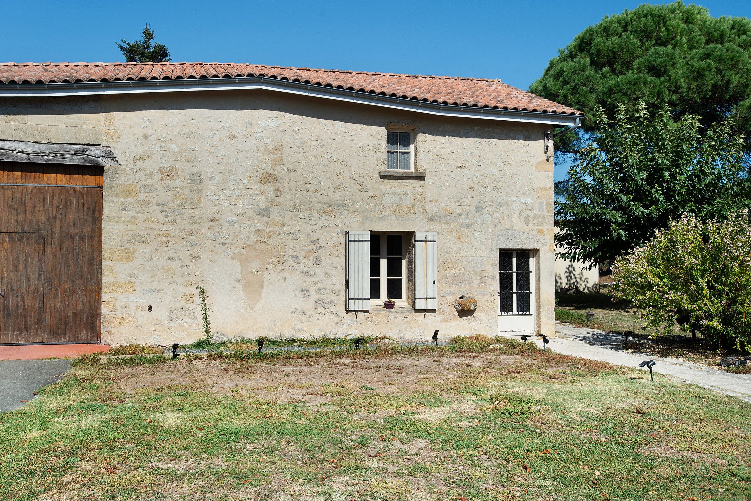 Un bâtiment en pierre à deux étages, avec un toit en tuiles, une porte en bois et des volets aux fenêtres.