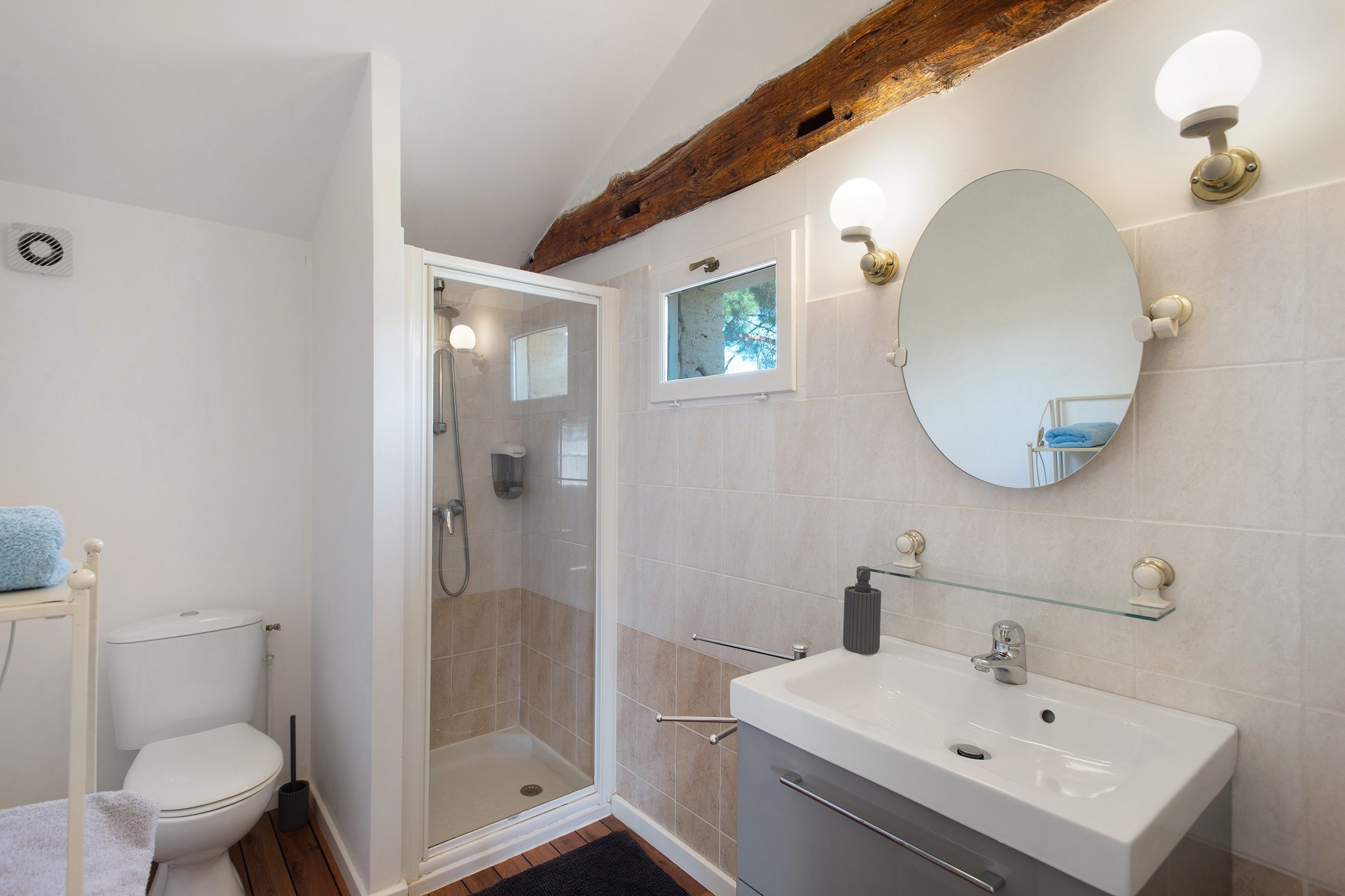 Une salle de bain dotée d’une douche à parois de verre, d’un lavabo blanc avec une étagère en verre et d’un miroir agrémenté de luminaires fixés au mur.