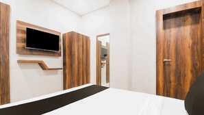 Un dormitorio con cama, televisor montado en la pared, armarios de madera y una puerta que da a otra habitación.