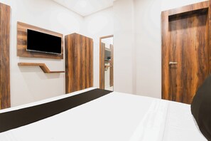 Ein Schlafzimmer mit einem Bett, einem an der Wand befestigten Fernseher, Holzschränken und einer Tür zu einem anderen Raum.