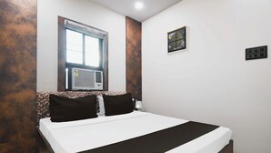 Habitación de hotel con cama, ventana, equipo de aire acondicionado, luz empotrada y toma de corriente.