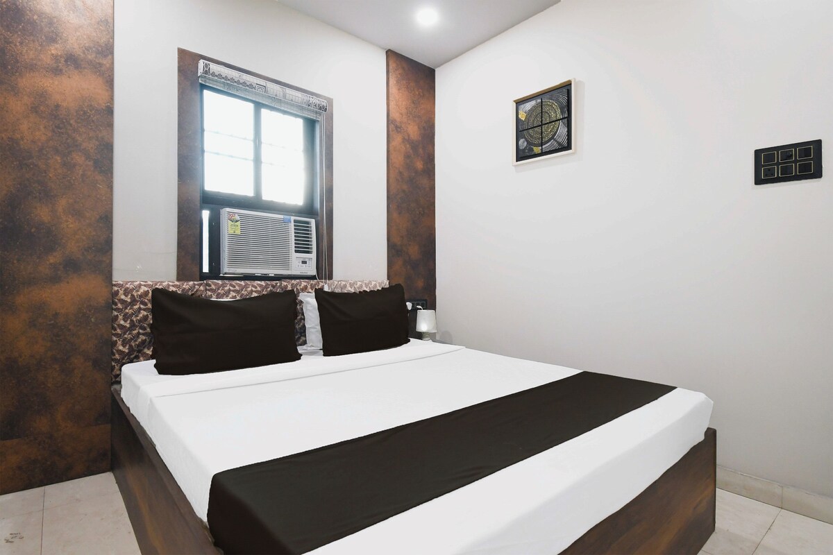 Ein Hotelzimmer mit Bett, Fenster, Klimaanlage, Wandleuchte und Steckdose.
