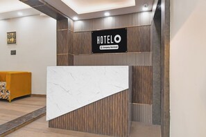 Ein Hotelrezeptionsschalter mit Marmortischplatte, Holzvertäfelung und einem Schild mit dem Hotelnamen.