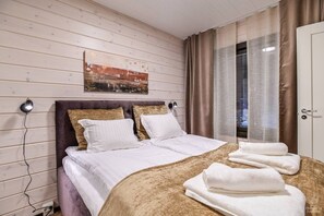 A hotel room with a wooden wall, a bed with white bedding, a headboard, and a window with curtains. - SointuiLevi Premium A71 by Holiday in Lapland (Levi)