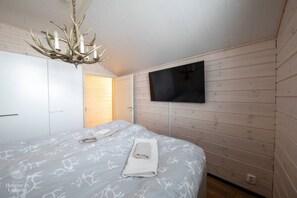 Ein Schlafzimmer mit einem Bett, einem an der Wand befestigten Fernseher und einer Holztür.