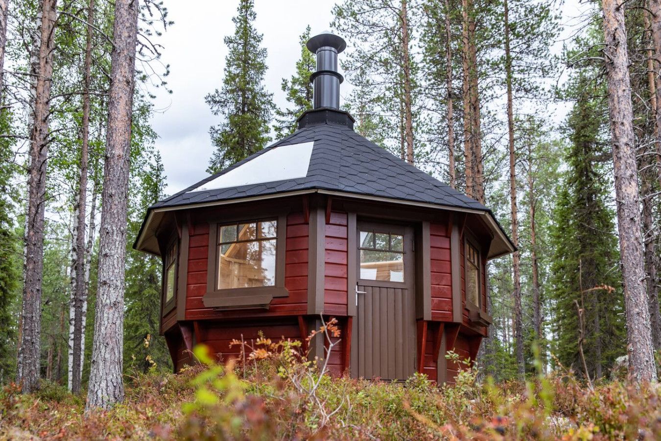 A small cabin with a chimney, surrounded by a forest.