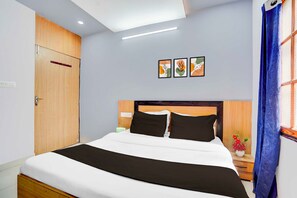 Habitación de hotel con cama, mesita de noche, lámpara de pared y ventana con cortinas.