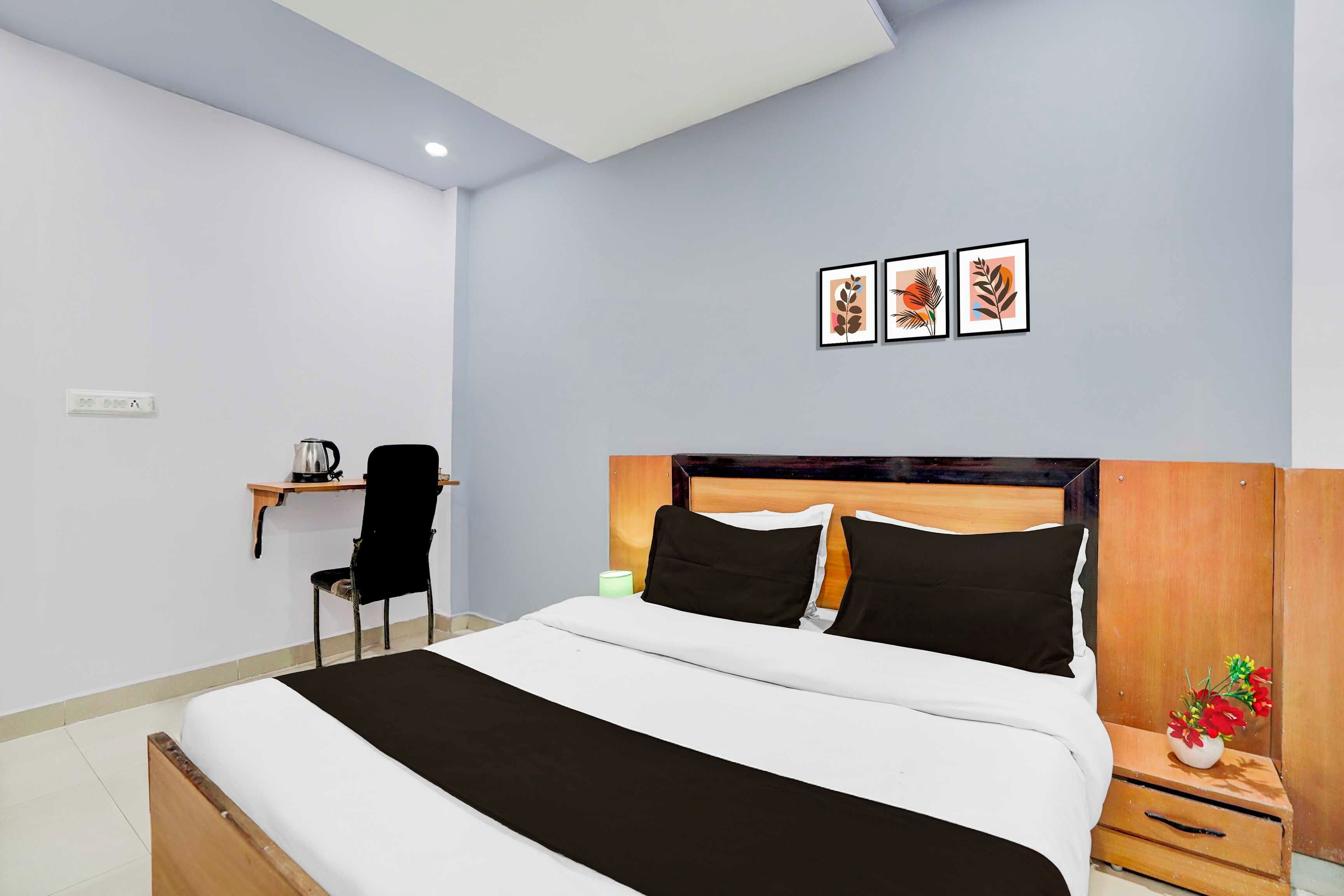 Un dormitorio con cama, mesita de noche, lámpara, silla y estante en la pared con una tetera.