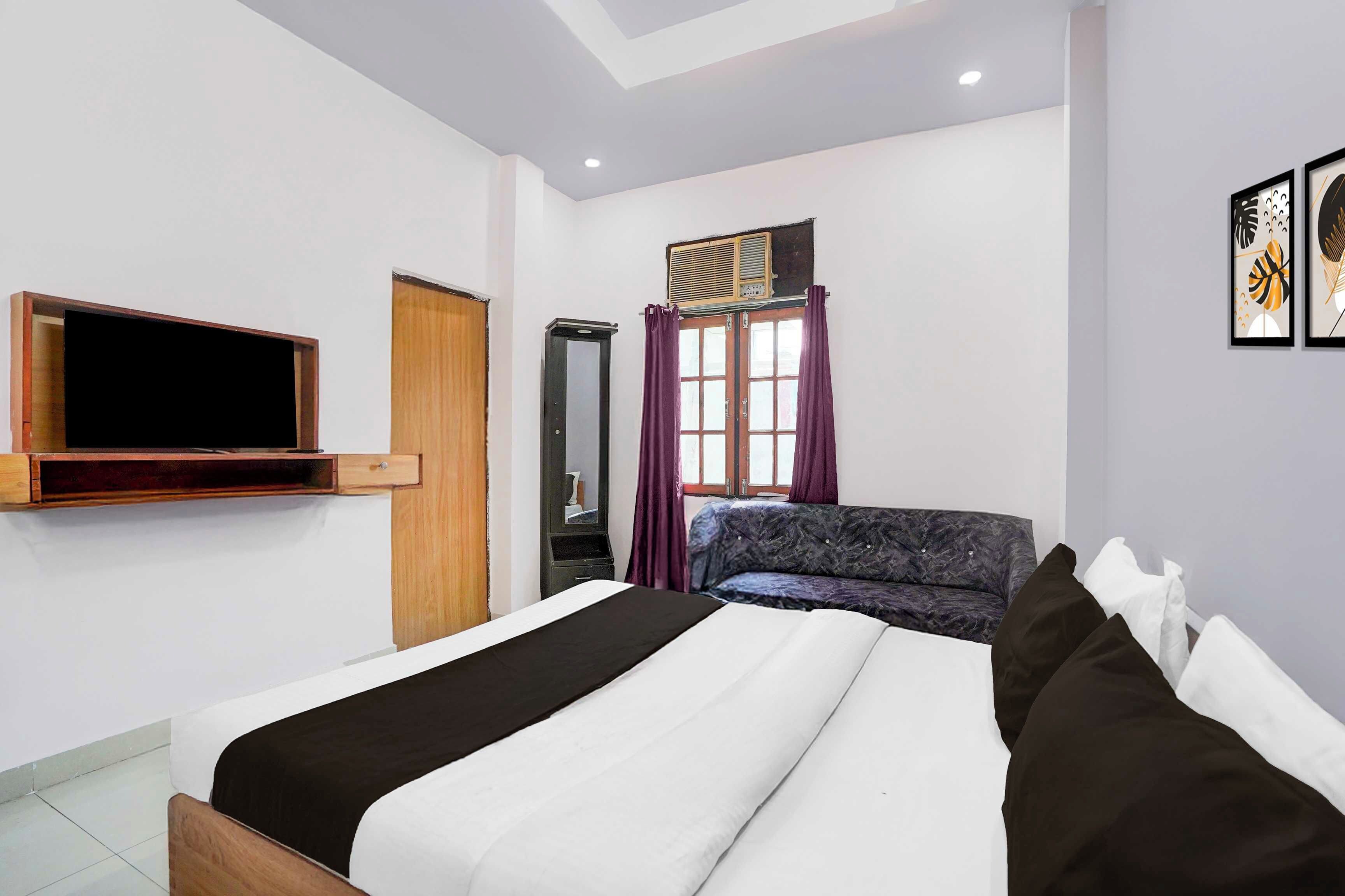A bedroom with a bed, a TV mounted on the wall, a wardrobe, and a window with curtains.