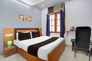Una habitación de hotel con cama, mesita de noche, lámpara, ventana con cortinas y una silla.