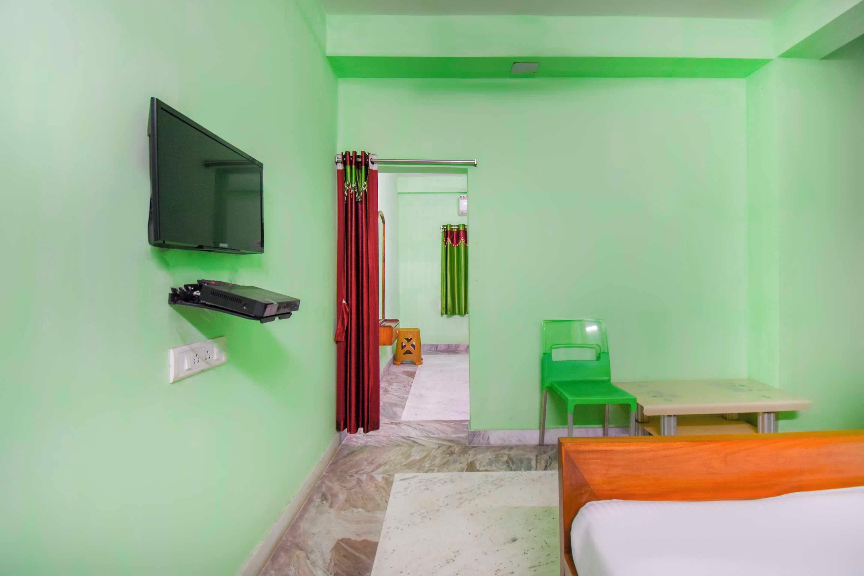 Una stanza con un letto, una scrivania, una sedia, una televisione montata a parete e un bagno visibile attraverso una porta aperta.