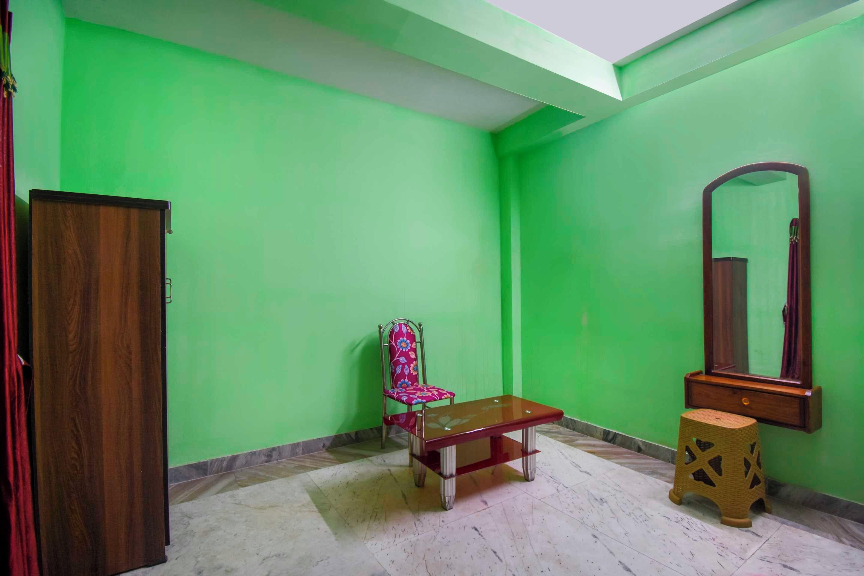 Una habitación con paredes verdes, un armario de madera, una silla, un banco, un taburete pequeño y un espejo en la pared.