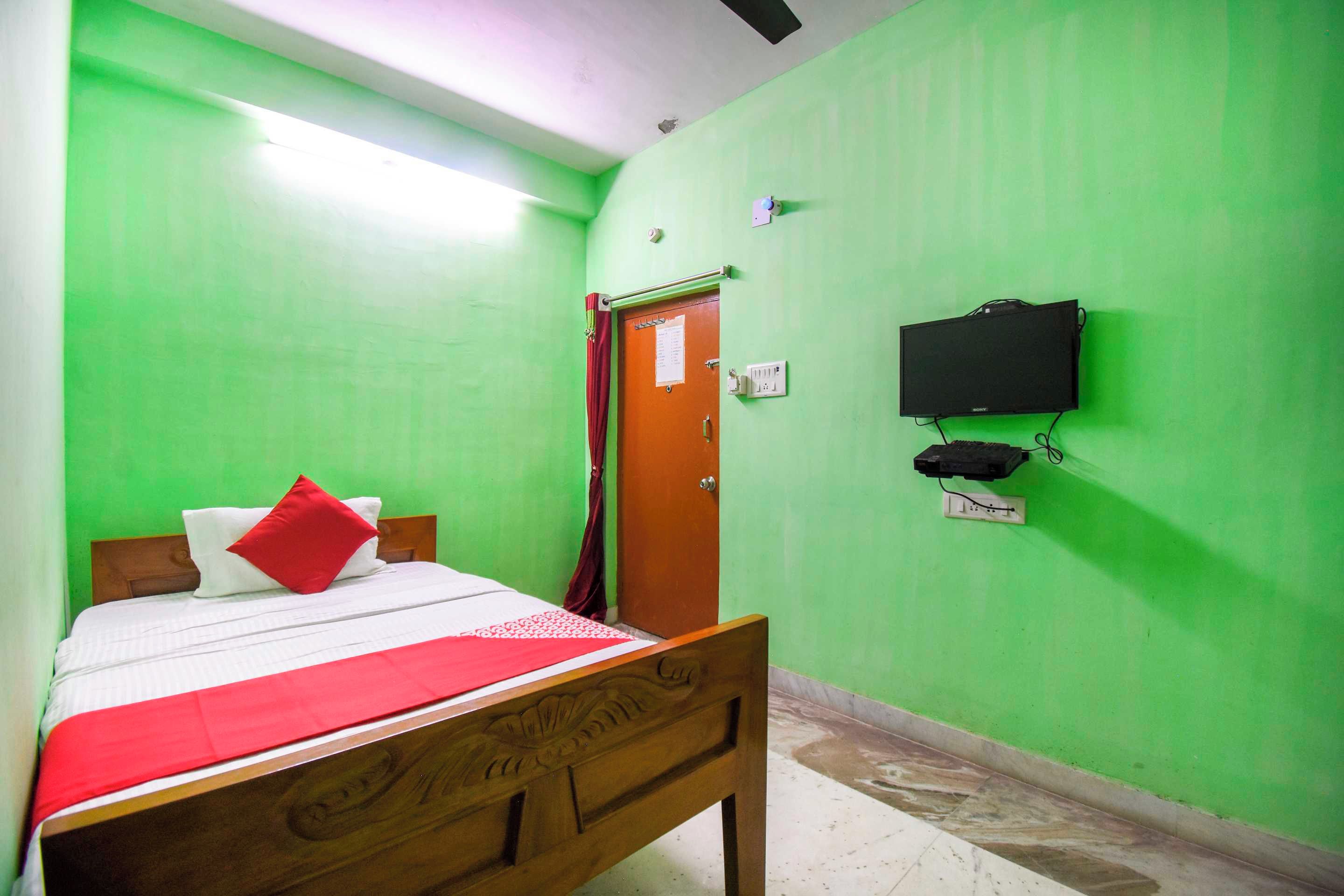 Una habitación con cama, puerta, televisor de pared y toma de corriente.